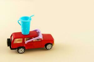rosso giocattolo auto su un' leggero sfondo nel occhiali da sole e un' bicchiere di morbido bevanda su il tetto con copia spazio foto