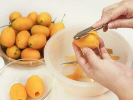 uomo sbucciare maturo succoso pelato marian prugna o prugna Mango al di sopra di bianca cucina sfondo, Tailandia fresco delizioso dolce asiatico famoso tropicale frutta foto