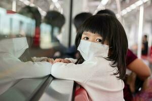 bambina con maschera chirurgica per la protezione del viso focolaio di virus e influenza nel trasporto pubblico skytrain o metropolitana. concetto di nuovo stile di vita normale, utilizzando i mezzi pubblici per recarsi a scuola. foto