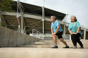 asiatico anziano coppie indossare gli sport attrezzatura e riscaldamento su muscoli prima esercizio a all'aperto nel il mattina. contento anziano all'aperto stile di vita concetto, pieno lunghezza di attivo contento anziano famiglia coppia foto