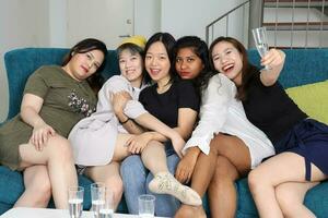 giovane asiatico donna gruppo parlare pettegolezzo Chiacchierare cantare bevanda Saluti festa divertimento godere divertente facce espressione su blu vivente camera divano foto
