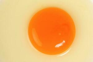 crudo uovo tuorlo e bianca liquido nel trasparente bicchiere ciotola bianca sfondo foto
