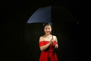 asiatico donna nel moderno rosso vestito sotto ombrello su nero sfondo foto