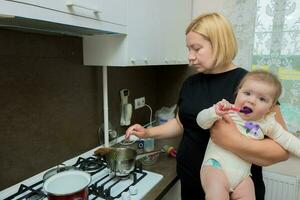 madre nel il cucina con un' bambino nel sua braccia preparazione cibo foto