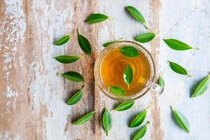 tazza di tè e foglie di tè fresche su un tavolo di legno foto