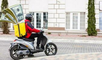 consegna uomo nel rosso berretto maglietta uniforme guida ciclomotore motocicletta scooter hold denaro contante i soldi isolato su giallo sfondo studio maschio dipendente Lavorando Corriere servizio quarantena pandemia covid-19 concetto. foto