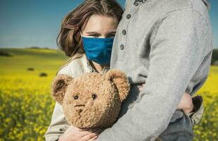 ragazza nel respirazione viso maschera abbracciare sua papà e orsacchiotto orso foto