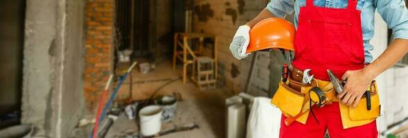 costruzione lavoratore a costruzione luogo con protettivo uniforme, costruzione servizio utensili e attrezzatura, tuta e detiene giallo casco, martello attrezzo, misurare nastro, spirito livello attrezzo nel mani. foto