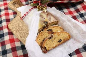 Natale natale decorazione ornamento campana regalo carta avvolgere affettato Stollen frutta torta cibo su di legno tavola verificato tessuto foto