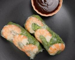 vietnamita gamberetto gamberetto vedere attraverso riso carta primavera rotolo verde verdura salsa su buio piatto foto