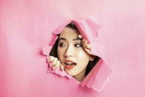 giovane bellissimo asiatico donna espressione attraverso strappato carta buco foto