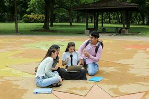 giovane asiatico malese Cinese uomo donna all'aperto parco sedersi su terra studia parlare discutere punto il computer portatile file libro zaino mescolarsi divertimento incontrare foto