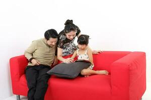 Sud est asiatico giovane coppia padre madre figlia genitore ragazza bambino su rosso divano leggere Scrivi studia libro su bianca sfondo foto