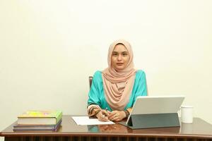 giovane asiatico malese musulmano donna indossare foulard a casa ufficio alunno sedersi a tavolo computer libro file carta studia opera foto