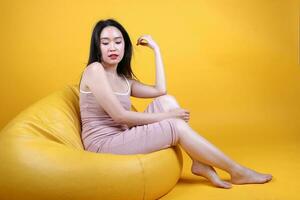 bellissimo giovane Sud est asiatico donna sedersi su un' giallo arancia beanbag posto a sedere colore sfondo posa moda stile elegante bellezza umore foto