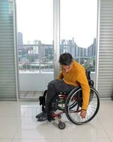 giovane uomo Sud est asiatico malese origine seduta su sedia a rotelle contro finestra luce. paralizzato vita giù dovuto per incidente foto