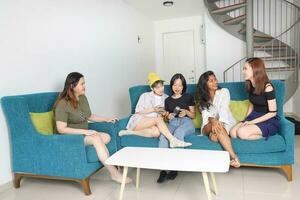 giovane asiatico donna gruppo parlare pettegolezzo Chiacchierare cantare festa divertimento godere emozione su blu vivente camera divano foto