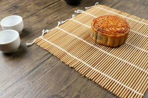 Cinese al forno decorato mooncake medio autunno Festival il giro Luna torta Riempimento regalo desiderio offerta su bambù stuoia al di sopra di di legno tavolo mini tazza foto