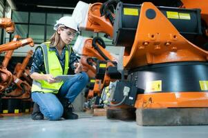 femmina tecnico ispezionando e riparazione robotica braccio nel robot hangar e test il operazione di il macchina dopo essere Usato per un' mentre, come bene come in aggiornamento il Software e calibrazione foto