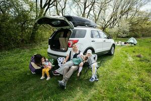 famiglia con bambini sedersi su sedia contro auto Aperto tronco su picnic. foto