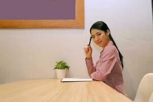 giovane Sud est asiatico donna attività commerciale ufficio a bar sedia tavolo Guarda a telecamera miglio Tenere penna foto