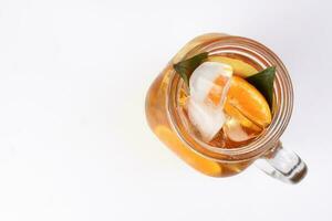 liquido ghiaccio Limone arancia tè con fetta verde foglia cannella bastone nel trasparente bicchiere vaso boccale su bianca sfondo superiore Visualizza foto