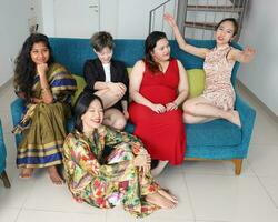 giovane asiatico donna gruppo parlare pettegolezzo Chiacchierare cantare fabbricazione divertente beffardo facce espressione su blu vivente camera divano sedersi su pavimento foto