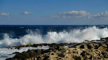 blu mare onda e bianca schiuma e spruzzata. pietra spiaggia su isola di Malta, no sabbioso spiaggia. estate vacanza confine telaio concetto. tropicale isola vacanza sfondo. turista viaggio bandiera design modello. foto