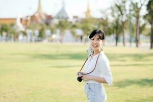 ritratto di asiatico donna viaggiatore utilizzando telecamera. Asia estate turismo vacanza concetto con il mille dollari palazzo nel un' sfondo a bangkok, Tailandia foto