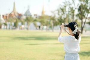 ritratto di asiatico donna viaggiatore utilizzando telecamera. Asia estate turismo vacanza concetto con il mille dollari palazzo nel un' sfondo a bangkok, Tailandia foto