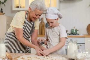 contento famiglia nel cucina. nonna nipotina bambino taglio biscotti di Impasto su cucina tavolo insieme. nonna insegnamento ragazzo ragazza cucinare infornare biscotti. domestico lavoro di squadra porzione famiglia generazioni. foto