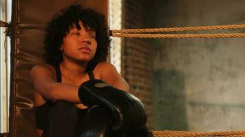 donna combattente ragazza potenza. africano americano donna combattente con boxe guanti seduta su boxe squillare in attesa e riposo dopo combattere. forte potente ragazza nel palestra. forza in forma corpo allenarsi addestramento. foto