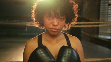 grido indipendente ragazza potenza. arrabbiato africano americano donna combattente con boxe guanti guardare grave aggressivo per telecamera in piedi su boxe squillo. forte potente ragazza guardare concentrato dritto. foto