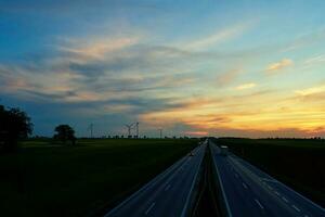 autostrada con auto traffico e mulino a vento turbine a tramonto foto