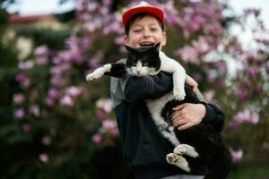 ragazzo nel berretto hold gatto nel mani contro simpatico primavera giorno vicino magnolia fioritura albero. foto