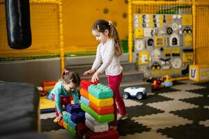 Due sorelle giocando a bambini giocare centro mentre costruire con colorato plastica blocchi. foto