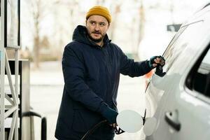 uomo rifornimento carburante il suo americano suv auto a il gas stazione nel freddo tempo atmosferico. foto