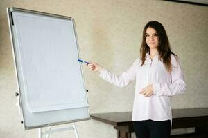 concentrato giovane caucasico altoparlante donna allenatore mostrare su bianca asse, preparazione o dando educativo conferenza. femmina squadra capo spiegando progetto idee. foto