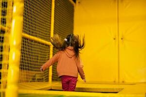 poco ragazza ragazzo salto su trampolino a giallo terreno di gioco parco. bambino nel movimento durante attivo divertimenti. foto