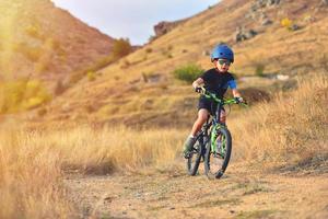 bambino felice ragazzo di 7 anni divertendosi nel parco in autunno con una bicicletta in una bella giornata autunnale bambino attivo che indossa il casco della bici foto