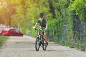 bambino felice che si diverte vicino a casa con una bicicletta in una bella giornata di primavera indossando una maschera protettiva per il virus pandemico covid19 del coronavirus