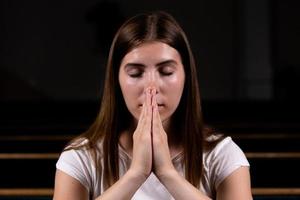 una ragazza cristiana in camicia bianca sta pregando con cuore umile nella chiesa foto