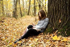 giovane bella ragazza in una giacca grigia che si siede nella foresta di autunno foto