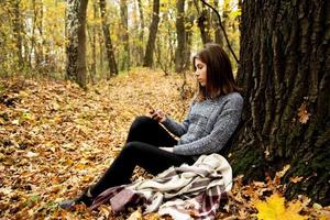 giovane bella ragazza in una giacca grigia che si siede nella foresta di autunno foto
