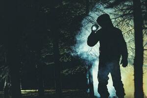 misterioso uomini con torcia elettrica nel il suo mano nel buio nebbioso foresta foto