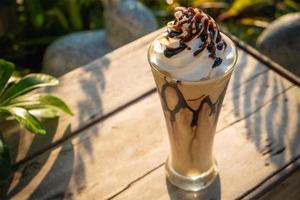 frappe al caffè con panna montata sul vecchio tavolo di legno al sole del mattino foto