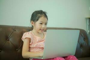 asiatico ragazza seduta su divano con computer godere giocando gioco foto