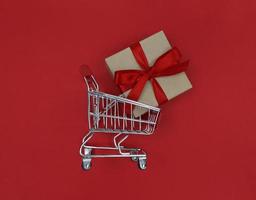 carrello del supermercato e confezione regalo su uno sfondo rosso il concetto di acquisto foto