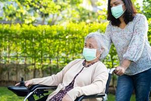 aiuta la donna anziana anziana o anziana asiatica su sedia a rotelle elettrica e indossa una maschera per proteggere l'infezione di sicurezza covid 19 coronavirus nel parco