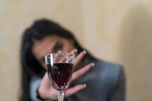 Rinunciando all'alcol una giovane donna al tavolo rifiuta un bicchiere di vino rosso con la mano foto